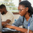 Young Nigerian university graduate filling out a scholarship application form on a laptop with documents beside them.