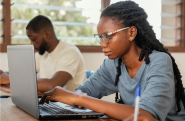 Young Nigerian university graduate filling out a scholarship application form on a laptop with documents beside them.
