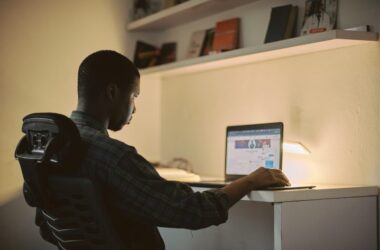 A Nigerian student studying at a desk while using a laptop for freelance work.