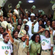 A group of NYSC corps members in Nigeria smiling and cheering while posing for a photograph with a distinguished figure