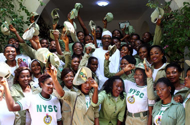 A group of NYSC corps members in Nigeria smiling and cheering while posing for a photograph with a distinguished figure