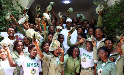 A group of NYSC corps members in Nigeria smiling and cheering while posing for a photograph with a distinguished figure